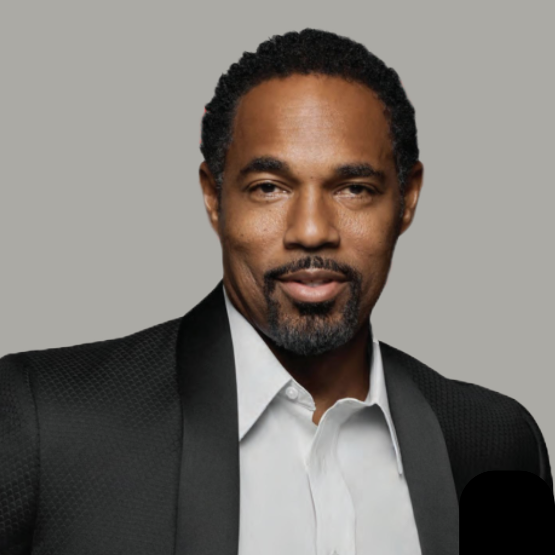 Image of Actor Jason George wearing a black suit jacket with white button down shirt. On a grey background